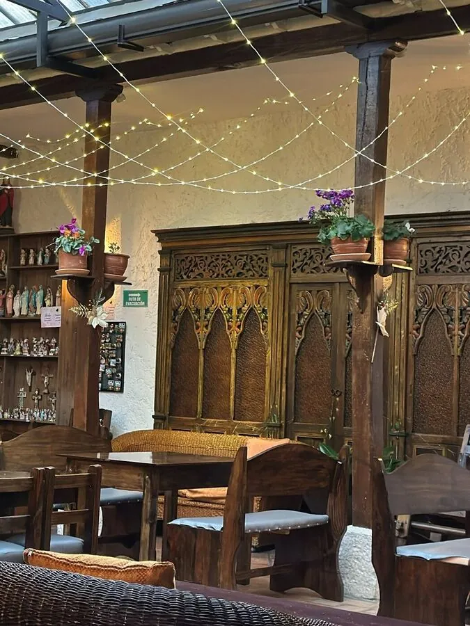 El salón de EUFORIA bajo el techo de vidrio: guirnaldas de luces, un armario de madera tallada, materas con flores y mesas de madera