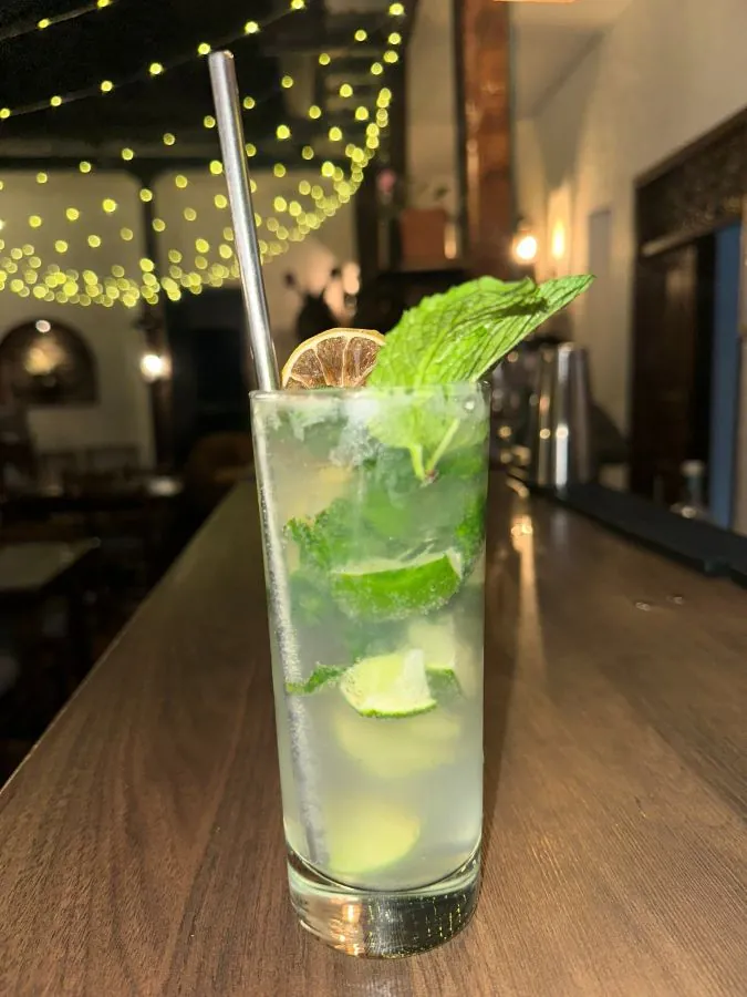Cóctel de hierbabuena y limón sobre la barra, con luces cálidas al fondo